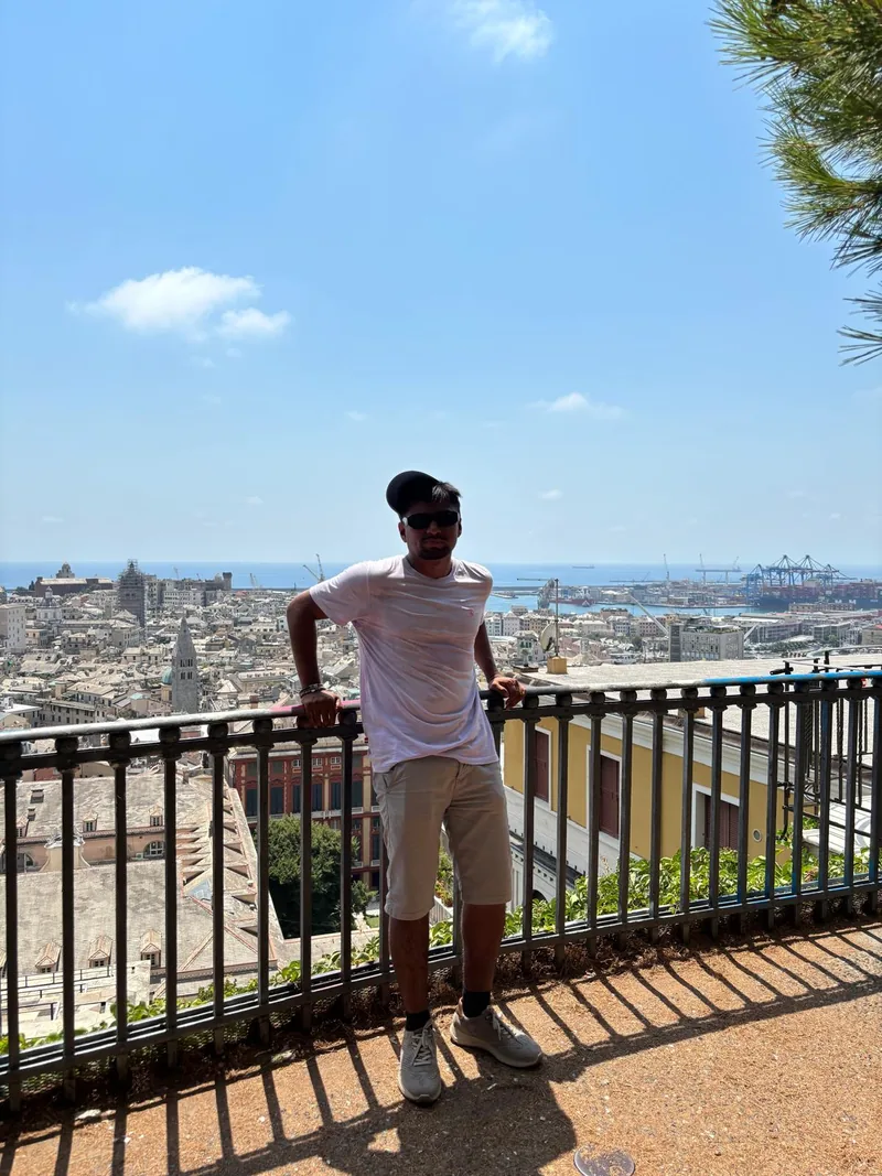 Alex apoyado en la barandilla de un mirador de Génova, con la ciudad y el puerto detrás